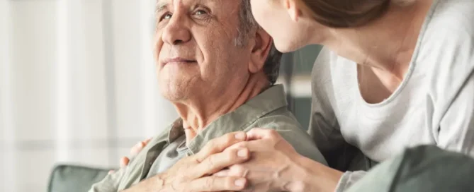 Adult daughter comforting her senior father at home in the late afternoon showing symptoms of sundowning