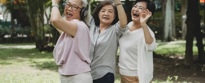 Three senior women dancing together in a park as part of social senior care solutions activities in Tacoma.